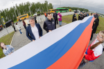На фото — патриотическая акция на трассе: большая группа людей развернула длинный флаг России на разделительной полосе автомагистрали, Изображение.