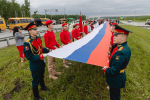 На фото — патриотическая акция на трассе: большая группа людей развернула длинный флаг России на разделительной полосе автомагистрали, Изображение.