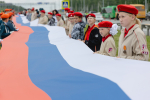 На фото — патриотическая акция на трассе: большая группа людей развернула длинный флаг России на разделительной полосе автомагистрали, Изображение.
