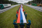 На фото — патриотическая акция на трассе: большая группа людей развернула длинный флаг России на разделительной полосе автомагистрали, Изображение.