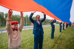 На фото — патриотическая акция на трассе: большая группа людей развернула длинный флаг России на разделительной полосе автомагистрали, Изображение.