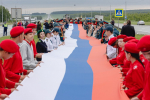 На фото – патриотическая акция на трассе: большая группа людей развернула длинный флаг России на разделительной полосе автомагистрали., Изображение.